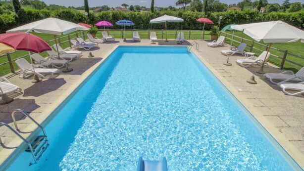 Une piscine rectangulaire à l’eau d’un bleu cristallin, entourée de chaises longues blanches et de parasols.