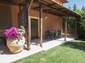 A covered patio with a table and chairs, a large flower pot, and a wooden door. - Trilocale by Interhome (Orentano)