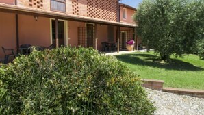 Un bâtiment à deux étages avec une façade en briques, un patio couvert doté de sièges extérieurs et un jardin bien entretenu.