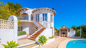 Una villa moderna con piscina, una escalera que lleva a un balcón y una zona de barbacoa.