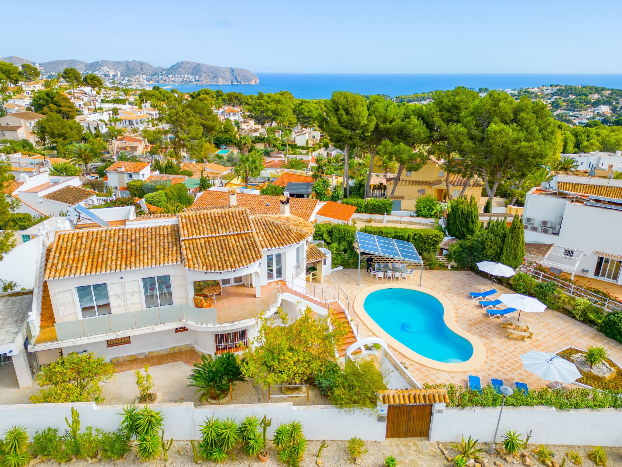 A residential property with a swimming pool, solar panels, and a view of the sea.