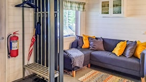 A cozy living room with a grey sofa, colorful cushions, a patterned rug, a fire extinguisher, and a window with a view of trees. - Pilkkaniemi by Interhome (Juuka)