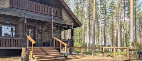 A cabin with a wooden deck, a staircase, and a view of a forest.