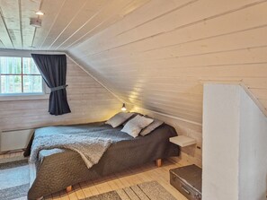 Et soveværelse med seng, et vindue med gardiner, en sengetavlelampe og en kuffert.