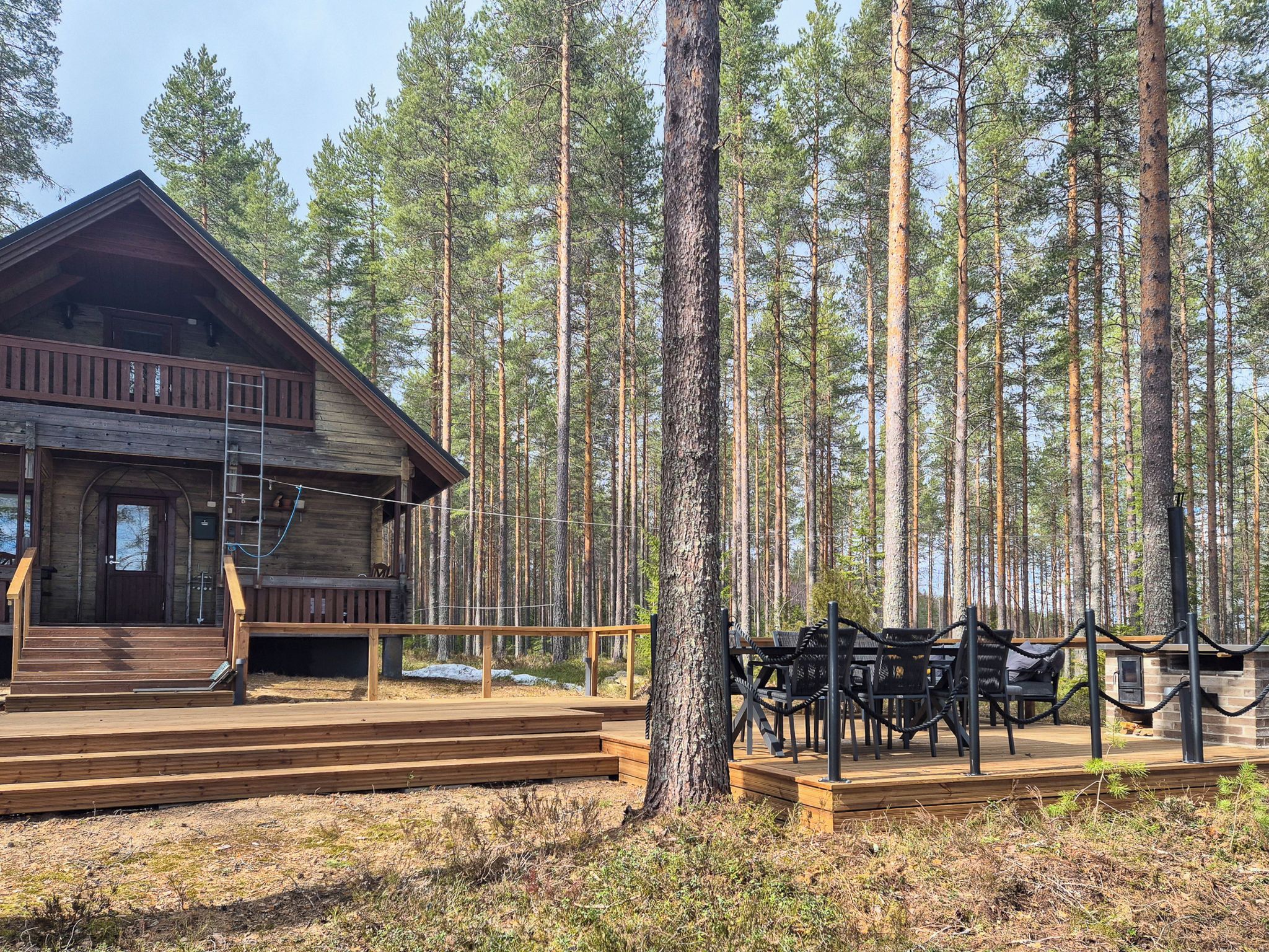 Une cabane en bois dotée d’un porche et d’un espace extérieur aménagé pour s’asseoir, le tout entouré de grands pins.