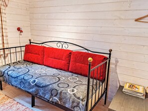 A metal-framed sofa with patterned upholstery, red cushions, and a small bedside table with a lamp.