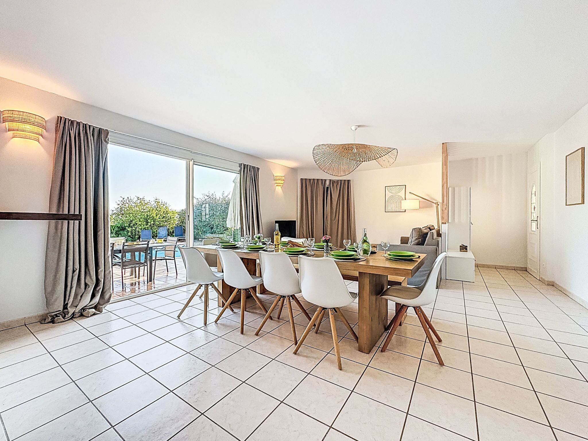 A modern dining area with a large table set for six, surrounded by white chairs. There is a large window providing a view of the outdoors.