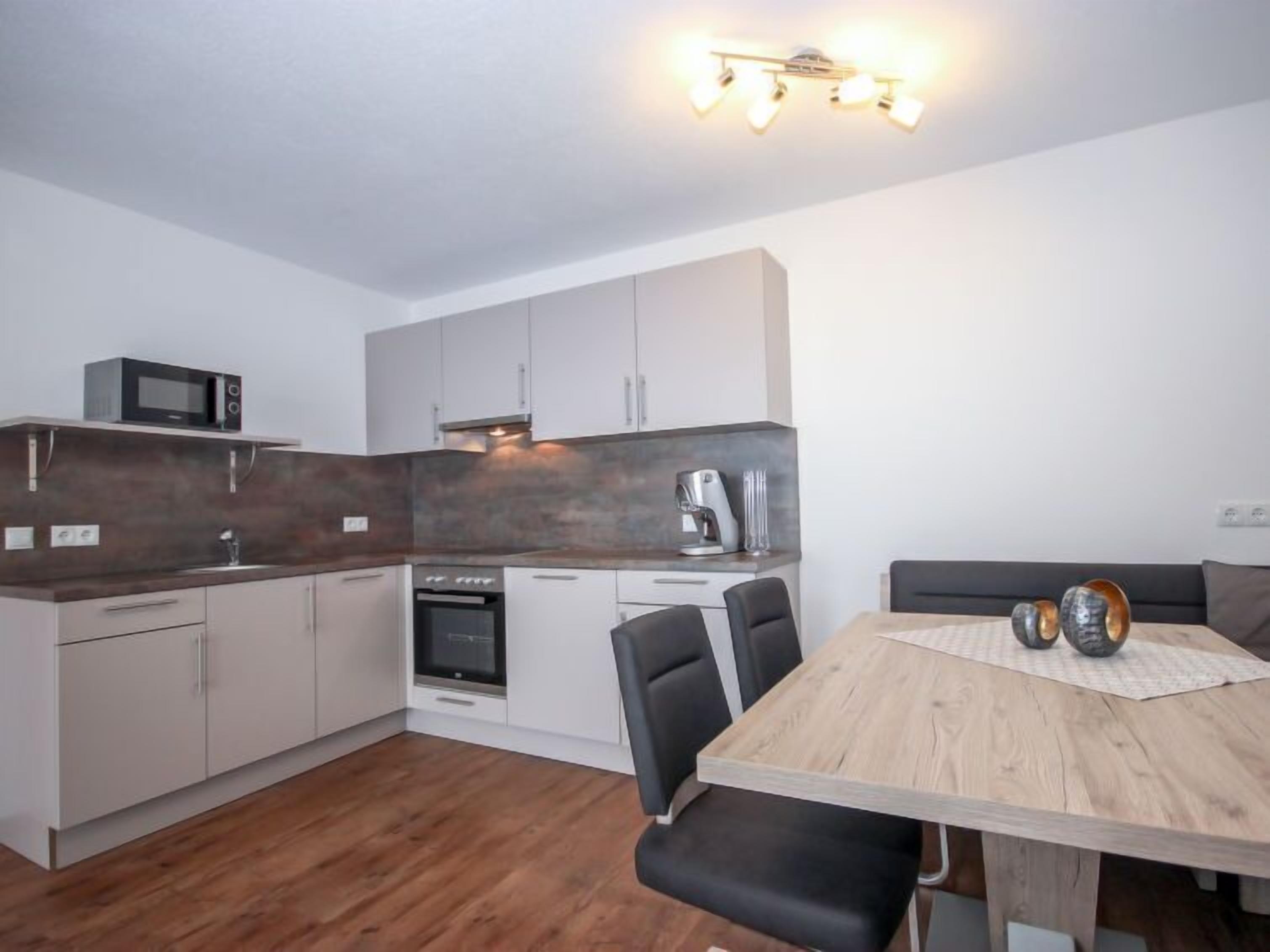Una cocina moderna con armarios blancos, microondas, cafetera y una mesa de comedor de madera con sillas.