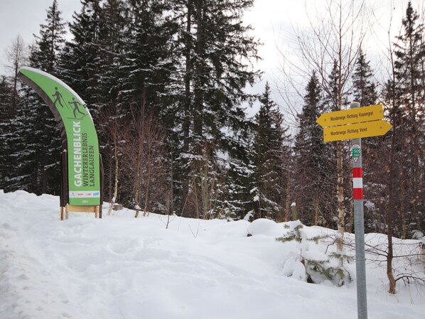 A snow-covered landscape with a sign indicating directions to Gachenblick Wintererlebnis Langlaufer and Wanderwege Richtung Kaunergrat and Richtung Venet.