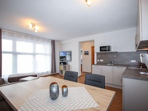 A modern living room with a wooden dining table, two grey vases, and a TV on the wall.