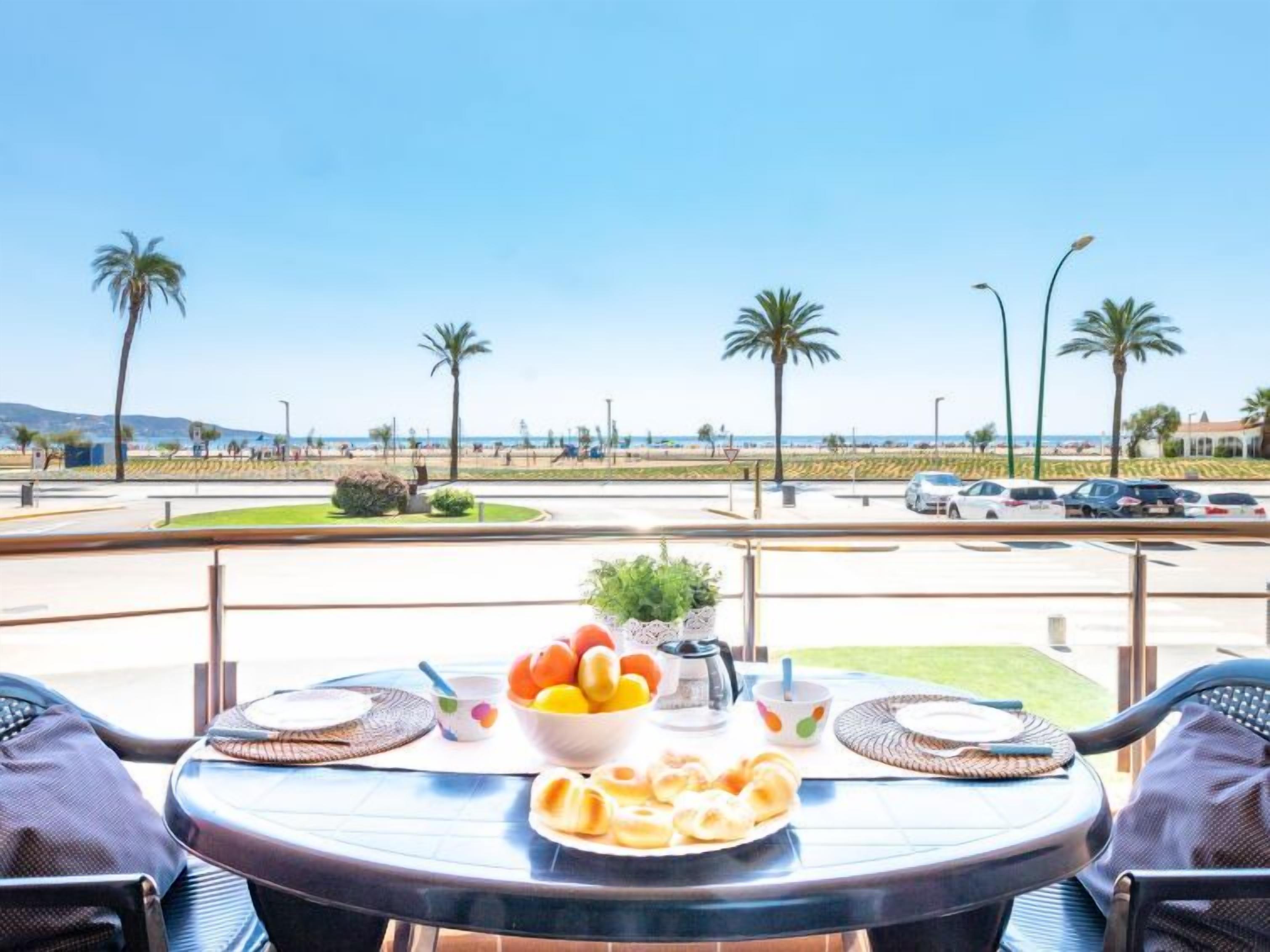 A table with breakfast items and a view of a beach and parking area.