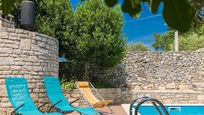 Un espace piscine avec des murs en pierre, deux chaises longues bleues et une chaise jaune.