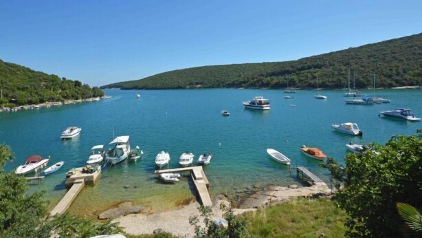 Un port de plaisance où sont amarrés des bateaux, entouré de collines et bordé d’une eau d’un bleu limpide.