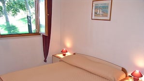 Une chambre à coucher avec un lit, deux tables de chevet avec des lampes, une fenêtre avec des rideaux et un tableau encadré au mur.