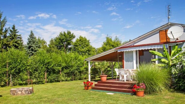 Ein Haus mit überdachter Veranda, Satellitenschüssel und einem kleinen Garten mit Topfpflanzen und Rasen.