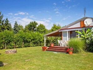 A house with a covered porch, a satellite dish, and a small garden with potted plants and a lawn. - Azzurro by Interhome (Balatonmariafurdo)