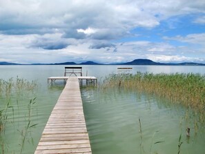 Eine Holzstege führt in einen ruhigen See, am Ende befindet sich eine Bank.