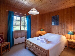 A wooden-paneled bedroom with a large bed, two bedside lamps, a window with curtains, and a radiator. - Chalet Lorila by Interhome (Villars)