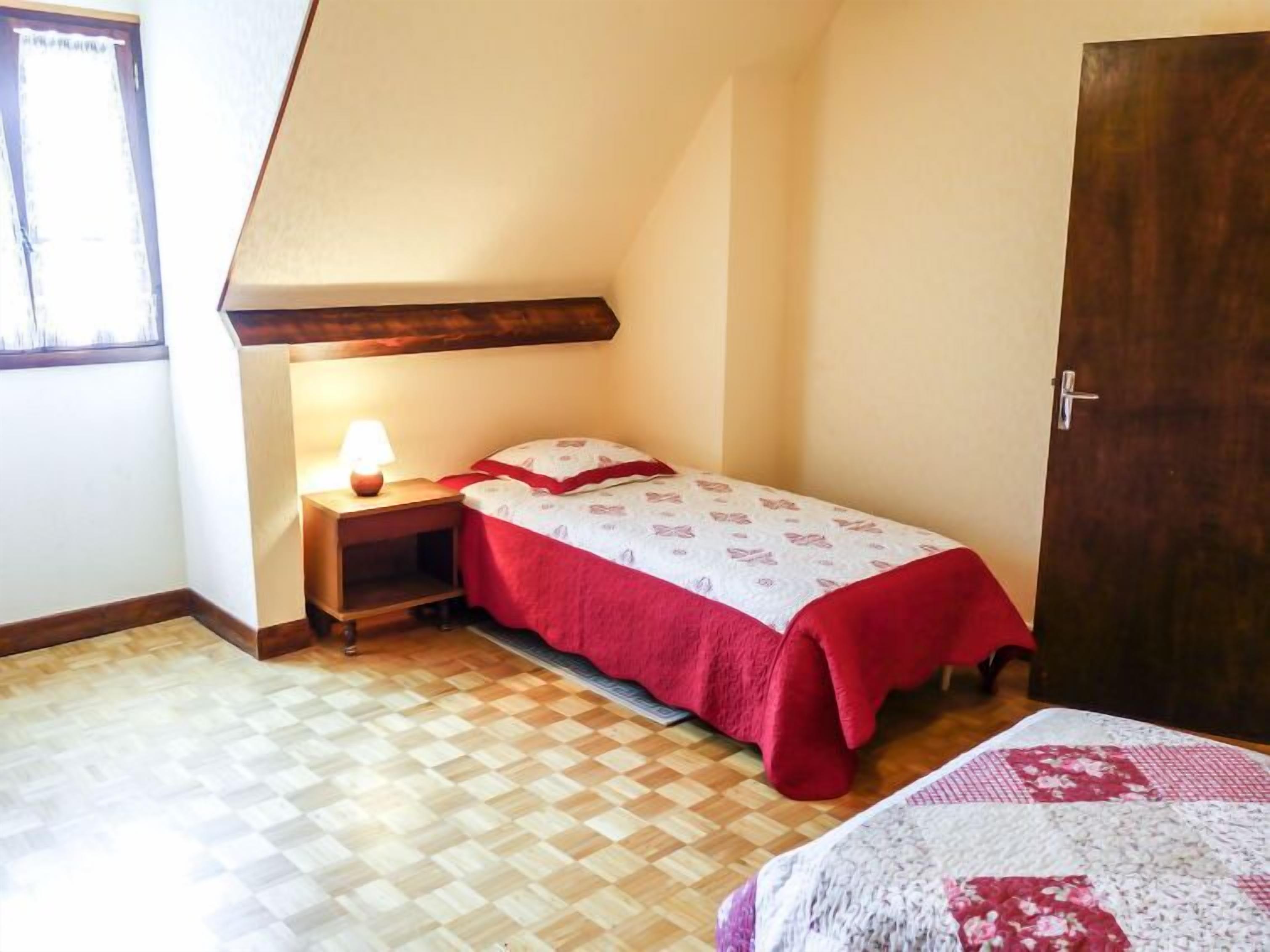 A small, cozy bedroom with a single bed, a nightstand with a lamp, and a wooden floor.