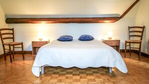 Ein Schlafzimmer mit Holzboden, einem Bett mit weißer Bettwäsche, zwei Nachttischen mit Lampen und zwei Holzstühlen.