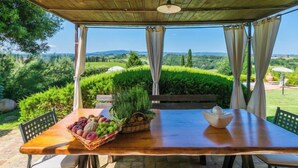 A wooden table with a fruit basket and a bowl, under a wooden pergola with a view of rolling hills and greenery. - Casa Mori by Interhome (Certaldo)