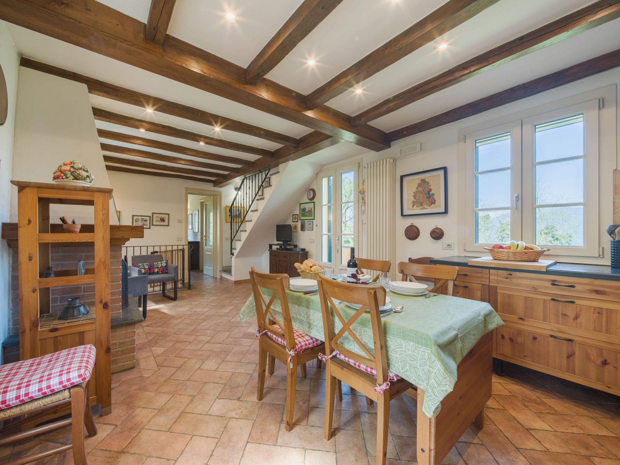 Une cuisine rustique avec des poutres en bois, un coin repas avec une nappe verte et un escalier menant à une autre pièce.