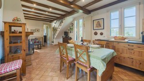 Une cuisine rustique avec des poutres en bois, un coin repas avec une nappe verte et un escalier menant à une autre pièce.