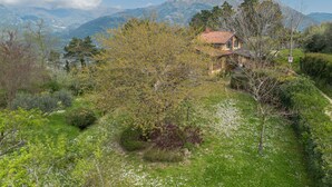 Une maison avec un toit recouvert de tuiles rouges, entourée d’une végétation luxuriante, et une montagne en arrière-plan.