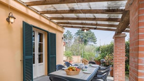 Une terrasse extérieure avec une table dressée pour le repas, entourée de chaises, et un mur de briques sur un des côtés.