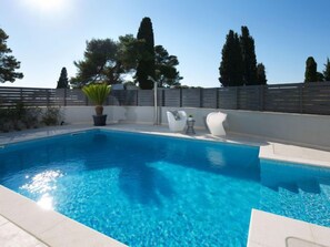 A clear blue swimming pool with a tiled deck, surrounded by a fence and trees. - Villa Fasana by Interhome (Fažana)