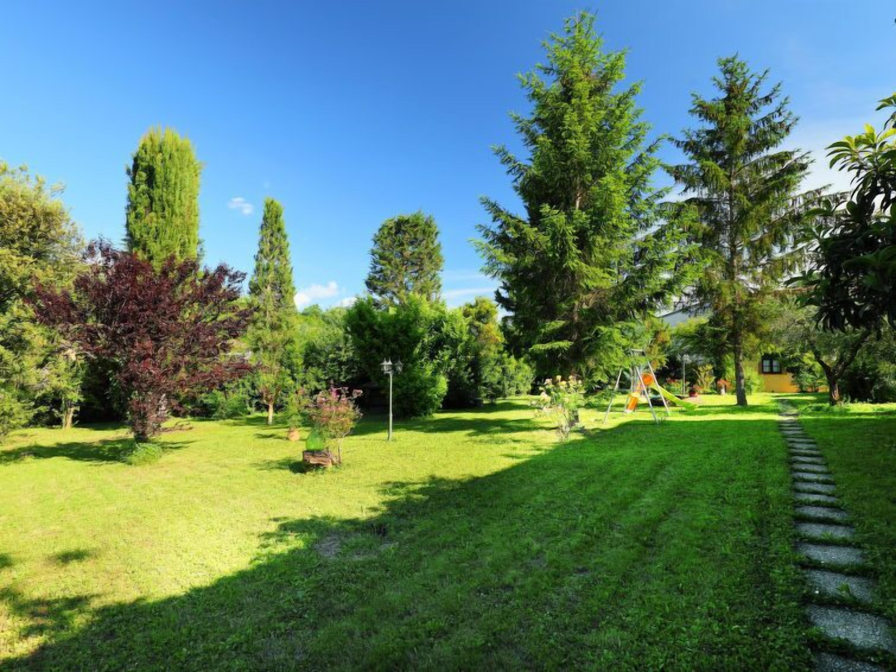 Un jardín bien cuidado con varios árboles, césped y un sendero de piedra.