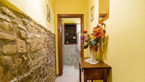 A hallway with a stone wall on one side and a yellow wall on the other, leading to a room with a tiled floor. - Il Gelsomino by Interhome (Montaione)