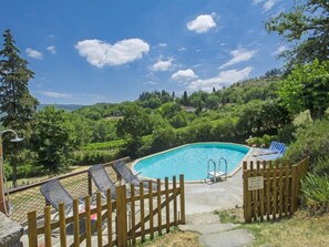 A swimming pool with a wooden fence and lounge chairs, surrounded by lush greenery and hills. - Le Bonatte by Interhome (Radda in Chianti)