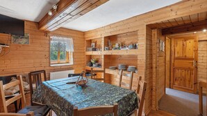 A cozy cabin interior with a dining table, chairs, a television, and wooden shelves. - Lenora I by Interhome (Lenora)