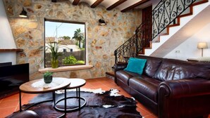 Uma sala de estar com parede de pedra, sofá de couro, tapete de couro, mesa de centro de madeira e escada com corrimão de ferro forjado.