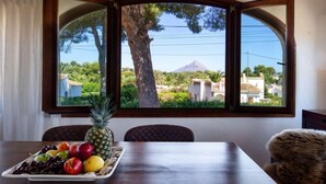 Uma mesa de jantar com um prato de frutas e vista para uma montanha através de uma janela em arco.