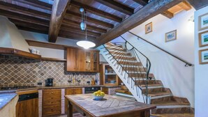 Cozinha rústica com piso de pedra, armários de madeira e escada de pedra.