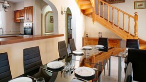 A dining area with a wooden table set for four, a kitchen in the background, and a staircase leading upstairs. - Somnium Mare by Interhome (Dénia)
