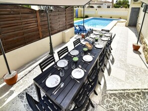 An outdoor dining area with a pool in the background.
