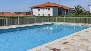 Una piscina con bordo piastrellato, circondata da un recinto bianco e un edificio con tetto rosso sullo sfondo.