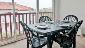 Zona pranzo con tavolo apparecchiato per quattro, una grande finestra con vista sugli edifici e un balcone con ringhiera rossa.