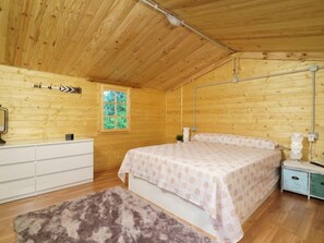 Une chambre dans une cabane en bois, avec un lit, une commode, une fenêtre et une table de chevet.