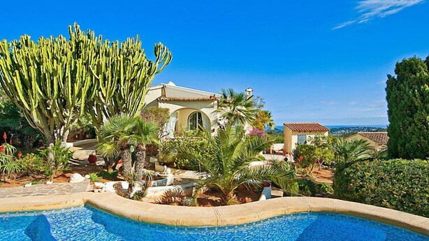 Ein Pool, umgeben von üppiger Vegetation und ein Gebäude im mediterranen Stil.