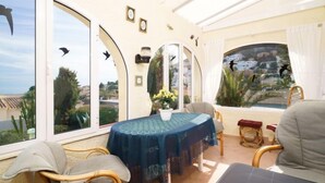 Eine sonnendurchflutete Terrasse mit Tisch und Stühlen, große Fenster mit Verzierungen und Blick auf die umliegende Landschaft.