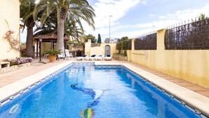 Piscina con sillas de descanso, palmeras y una pared amarilla.