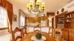 Un comedor con mesa y sillas de madera, una araña y una cocina al fondo.