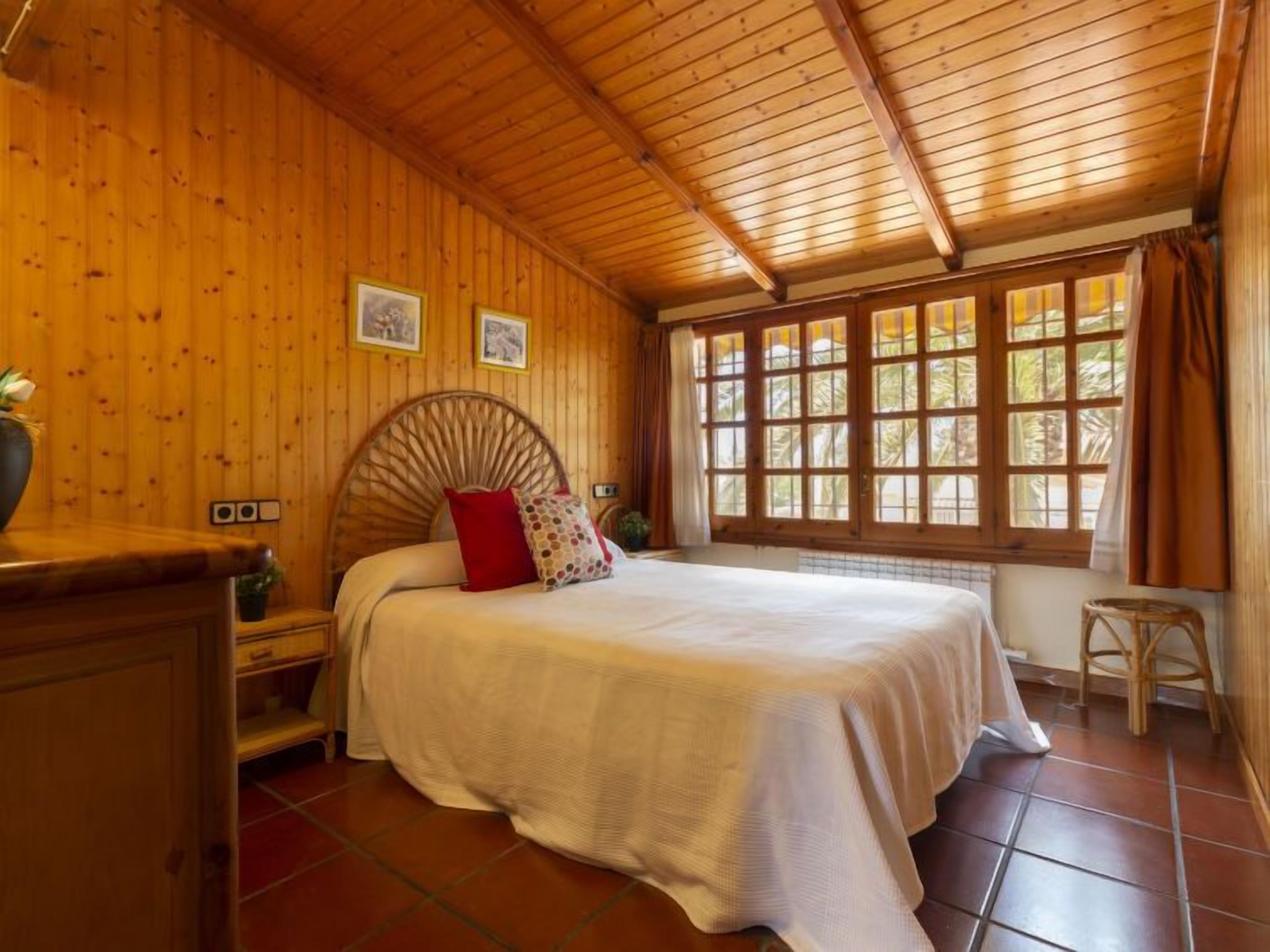 A wooden room with a bed, a window, and a small stool.