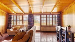 Una habitación acogedora con techo de madera, un sofá, una mesa de comedor con sillas y ventanas grandes con cortinas.