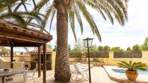Un patio exterior con pérgola, mobiliario, una palmera, una piscina y un farol.
