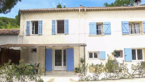Un edificio su due piani con persiane blu, un ingresso coperto e un’area giardino con piante.